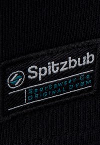 Schwarzes Stoffetikett mit "Spitzbub Sportswear Co." in weißer und türkisfarbener Stickerei, mit strukturiertem Hintergrund und subtilen Rillen.
