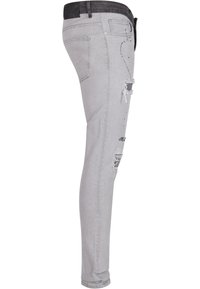 Lys grå smale jeans med et slitt design, som har rifter på låret, svart linning og subtile broderidetaljer.