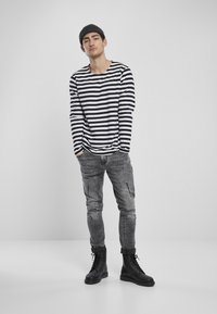 Zwart-wit gestreepte lange mouwen shirt, grijs versleten slim-fit jeans en zwarte veterschoenen. Eenvoudig minimalistisch ontwerp.