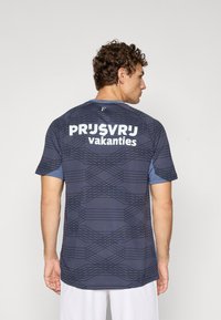 Camisola desportiva de manga curta em azul escuro com padrão geométrico e mangas azul claro contrastantes; apresenta texto branco na parte de trás.
