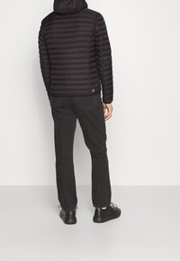 Černá prošívaná péřová bunda s kapucí a vodorovným prošíváním, nošená s černými kalhotami a černou obuví. Hladká textura, minimalistické detaily.