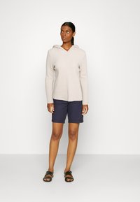 Beige Kapuzenpullover mit geripptem Stoff, kombiniert mit marineblauen Shorts und schwarzen Sandalen. Einfaches, lässiges Outfit-Design.