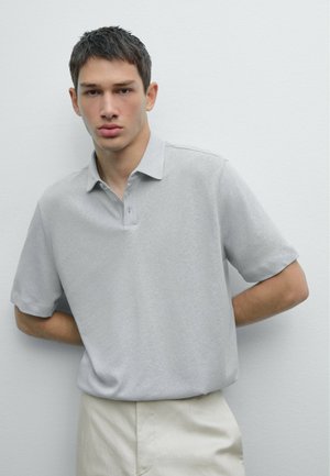 Polo à manches courtes en gris clair, en coton doux, avec une patte de boutonnage et un col classique, associé à un pantalon beige.