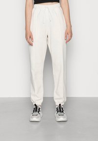 Person som bär ljusbeige joggerbyxor med elastiska muddar och dragsko i midjan, i kombination med vita och grå klumpiga sneakers.