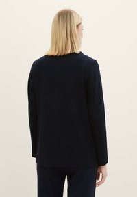Námořnický blazer s přiléhavým střihem, textilní tkaninou, dlouhými rukávy a rovnými lemy. Obsahuje minimalistické detaily a upravenou siluetu.