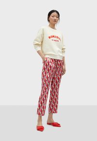 Felpa crema con la scritta "BONJOUR" in lettere rosse, abbinata a pantaloni a sigaretta rossi e rosa con motivi geometrici. Ballerine rosse completano il look.