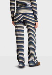 Gestreepte gebreide lounge set met wijde broekspijpen; bevat marineblauwe, gouden en zilveren strepen. Zachte textuur en ribbels aan de mouwen en taille.