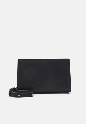 Portefeuille en cuir noir avec logo en relief, de forme rectangulaire, fermeture éclair et sangle de poignet détachable ornée de clous pour accent.