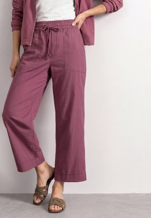 Femme portant un pantalon large mauve avec taille élastique et cordon, associé à une veste assortie et des sandales taupe slip-on.