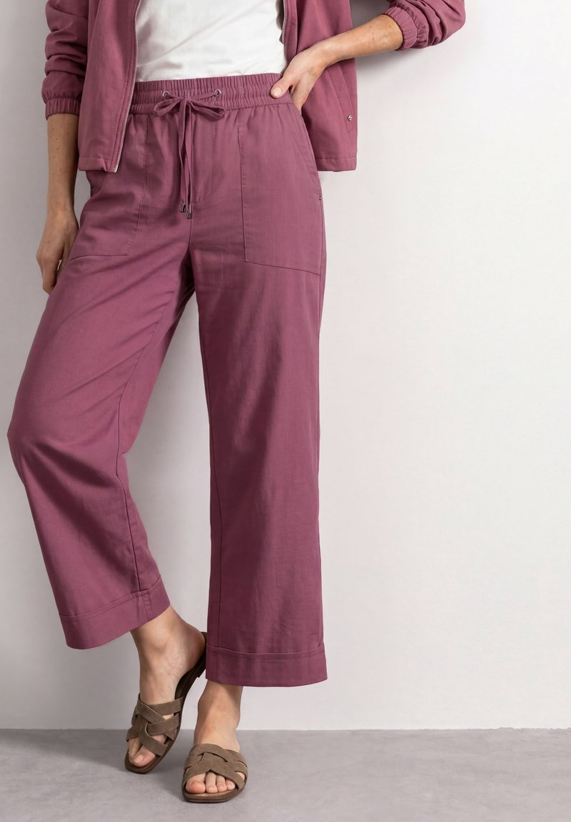 Femme portant un pantalon large mauve avec taille élastique et cordon, associé à une veste assortie et des sandales taupe slip-on.