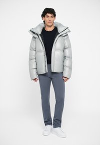Silver puffer jacket with a high collar, two front pockets, and quilted texture. Worn over a black top and paired with grey pants and white sneakers.