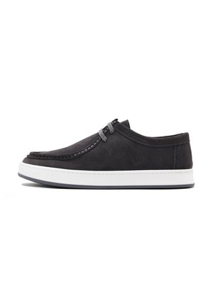 Zapatilla de ante negra con suela de goma blanca, que presenta costuras contrastantes y detalle de cordones para un ajuste seguro. Diseño minimalista.