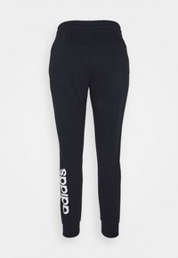 Pantalones de chándal azul marino con cintura elástica, piernas ajustadas y el logo blanco de "adidas" impreso a lo largo del lado izquierdo. Textura suave.