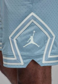 Šviesiai mėlynos krepšinio šortai, pagaminti iš tinklinės medžiagos, su dantyta apdaila ir baltais akcentais, bei Jumpman logotipu šone.