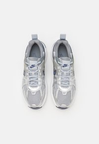 Nike sneakers featuring a mesh upper in grey with silver accents, white sole, lace-up design, and a logo on the tongue.