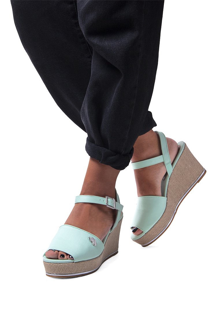 Mint vihreät viistokorkoiset sandaalit avosuun kanssa, nilkkahihna ja kudottu tekstuuri korkolapussa. Edessä koristeellinen emblem.