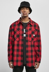 Rød og sort ternet flannel skjorte med to brystlommer og sorte knapper, båret over en sort grafisk T-shirt, parret med en sort bucket hat.