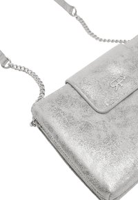 Srebrna metaliczna torebka na ramię z teksturowanym wykończeniem, klapą zamykaną oraz srebrnym łańcuszkiem. Z przodu znajduje się wytłoczone logo.