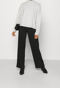 Maglione grigio a collo alto lavorato a maglia con polsini a coste, abbinato a pantaloni neri a gamba larga e stivali neri alla caviglia, con una borsa nera.