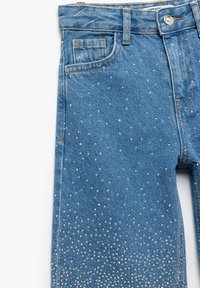 Blå denimjeans med spridda rhinestones, femficksdesign och rak benform med en lätt urtvättad look.