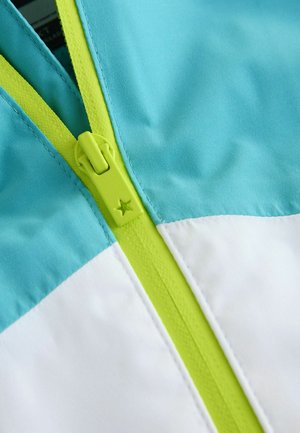 Bunda s modrou horní částí, bílou dolní částí a limetkově zeleným zipem se zajímavým hvězdovým detailem, vyrobená z hladké, lehké tkaniny.