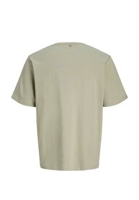 Ανοιχτό μπεζ κοντομάνικο μπλουζάκι, εμφανιζόμενο από πίσω με μια μικρή ετικέτα κοντά στη γραμμή του λαιμού σε λευκό φόντο.