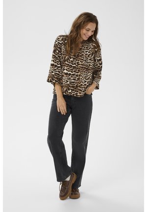 Haut à imprimé léopard marron et noir avec des manches larges, associé à un jean noir et des chaussures marron avec lacets et semelle épaisse.