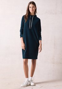Abito cappuccio in corduroy verde acqua con maniche lunghe, orli con risvolto, collo con cordoncino e una vestibilità morbida, abbinato a sneakers bianche e calzini alla caviglia.