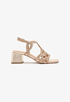 Sandal in rosa dorato metallizzato con intrecci e tacco a blocco quadrato, dotata di cinturino alla caviglia regolabile. Il design open toe mette in risalto dettagli intricati delle cinghie.