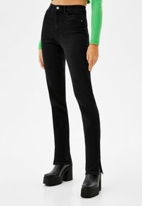 Svarta högmidjade jeans i slim fit med slitsar på fållen, tillverkade av denim. Matchad med kraftiga svarta platåstövlar.