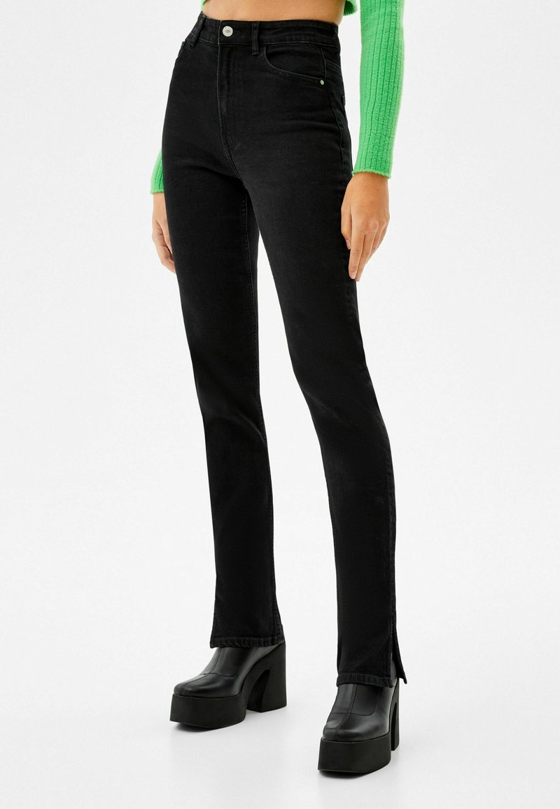 Svarta högmidjade jeans i slim fit med slitsar på fållen, tillverkade av denim. Matchad med kraftiga svarta platåstövlar.