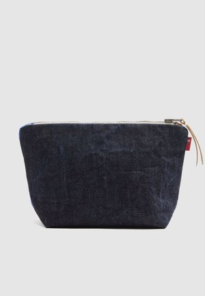 Klein donkerblauw denim portemonneetje met een leren trekker aan de rits, afgebeeld tegen een eenvoudige lichte achtergrond.