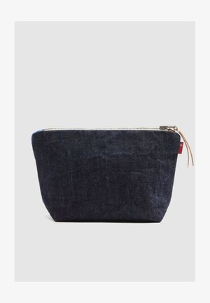 Kleine dunkelblaue Denim-Reißverschlusstasche mit einem Leder-Ziehgriff am Reißverschluss, auf schlichtem hellem Hintergrund.