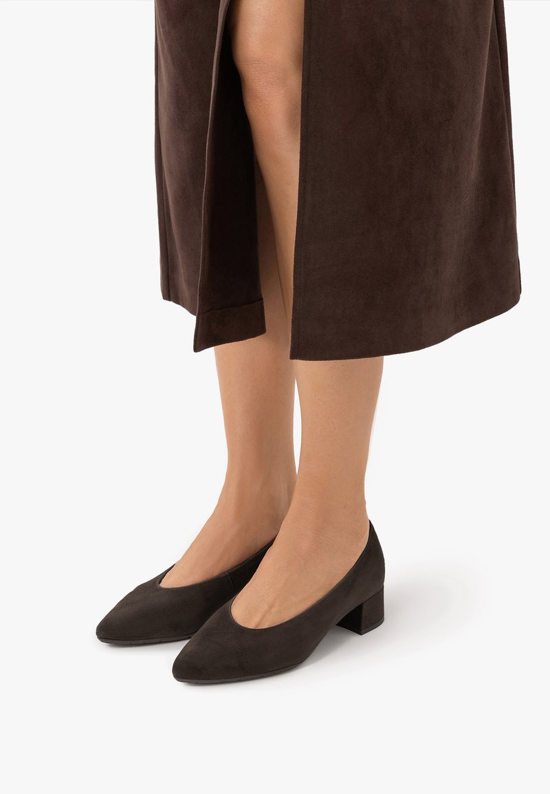 Jambes portant des chaussures à talons blocs bas en suède noir avec des bouts pointus et une jupe mi-longue marron avec une fente devant.