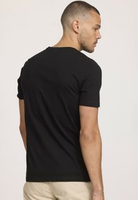 T-shirt noir à manches courtes avec un col rond et un tissu doux. Présente une silhouette ajustée et une texture lisse. Design uni sans motifs.