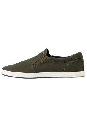Rentomainen slip-on-kengä öljynvihreästä kankaasta, valkoisella pohjalla ja pienellä punaisen, valkoisen ja sinisen logolla lähellä joustavaa sivupaneelia.