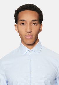 Camisa de vestir a cuadros azul claro hecha de algodón, con cuello clásico y parte delantera abotonada. Logo sutil en el pecho.