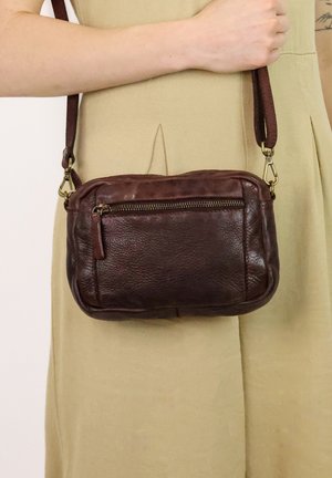 Sac bandoulière en cuir brun avec une surface texturée, poche zippée et bandoulière réglable. Présente une forme douce et arrondie avec un minimum de matériel.