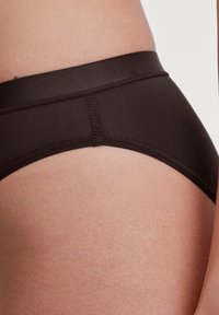 Mutande nere senza cuciture con texture liscia e vita elastica, angolate ai fianchi. Design minimalista, senza motivi o accessori visibili.