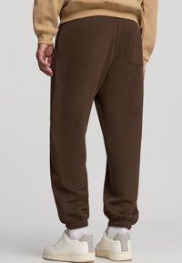 Brązowe bawełniane dresy z elastycznymi mankietami, z bocznymi kieszeniami i tylną kieszonką, w połączeniu z białymi trampkami i skarpetkami do kostek.