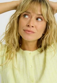 Cardigan amarillo claro hecho de un tejido suave y texturizado con un diseño acanalado y botones perlados a lo largo del frente.