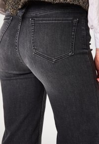 Jean en denim gris avec une taille haute, des poches arrière et une texture lisse légèrement décolorée. Aucun détail de matériel visible.