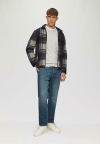Grau und marineblau kariertes Jackett mit Kapuze, grauer Pullover darunter, hellblaue Jeans und weiße Sneakers. Glattes Material und lässige Passform.