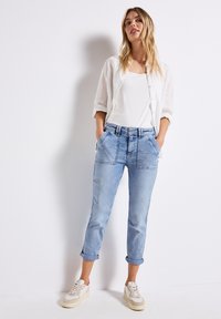 Jean en denim bleu clair avec une coupe droite, des poignets retroussés et des poches avant. Associé à un débardeur blanc et une chemise blanche transparente à boutons.