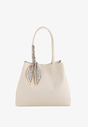 Sac cabas de couleur crème avec de longues poignées, orné d'un foulard noué à motif floral sur une des poignées, présenté sur fond blanc.