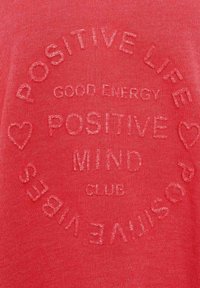 T-shirt rossa in cotone misto con testo in rilievo: "VITA POSITIVA, ENERGIA BUONA, CLUB DELLA MENTE POSITIVA" con cuori decorativi attorno al design.