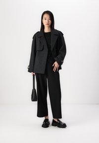 Manteau en laine mélangée oversize charbon avec de grandes poches et des boutons croisés, associé à un top noir en sequins et à un pantalon large. Des mocassins noirs robustes et un petit sac à main complètent le look.