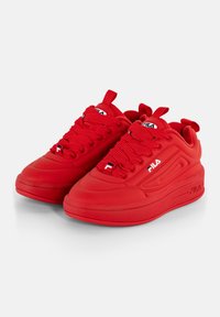 Un paio di sneakers FILA rosse con suole spesse, cuciture dettagliate e loghi brandizzati sui lati e sulle linguette, posizionate su una superficie bianca.