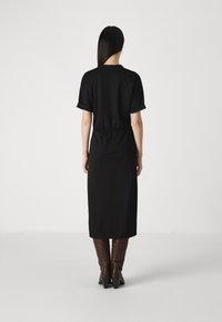 Vestido preto midi com mangas curtas dobradas, detalhe de cintura elástica e silhueta reta, combinado com botas castanhas até ao joelho.