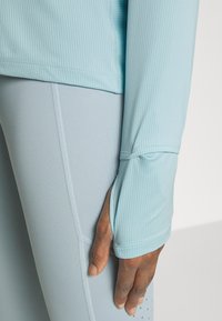 Himmelblaues Langarmoberteil mit geripptem Muster, hoch geschnittenen Bündchen, kombiniert mit himmelblauen Leggings und einer seitlichen Nahtdetails.